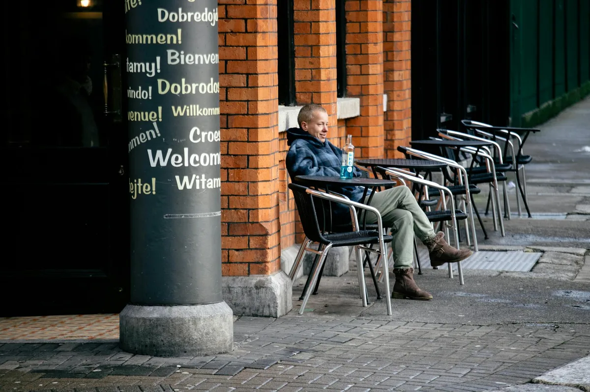 A person enjoys a peaceful morning sitting outside a café with multilingual welcome signs and urban brick architecture.