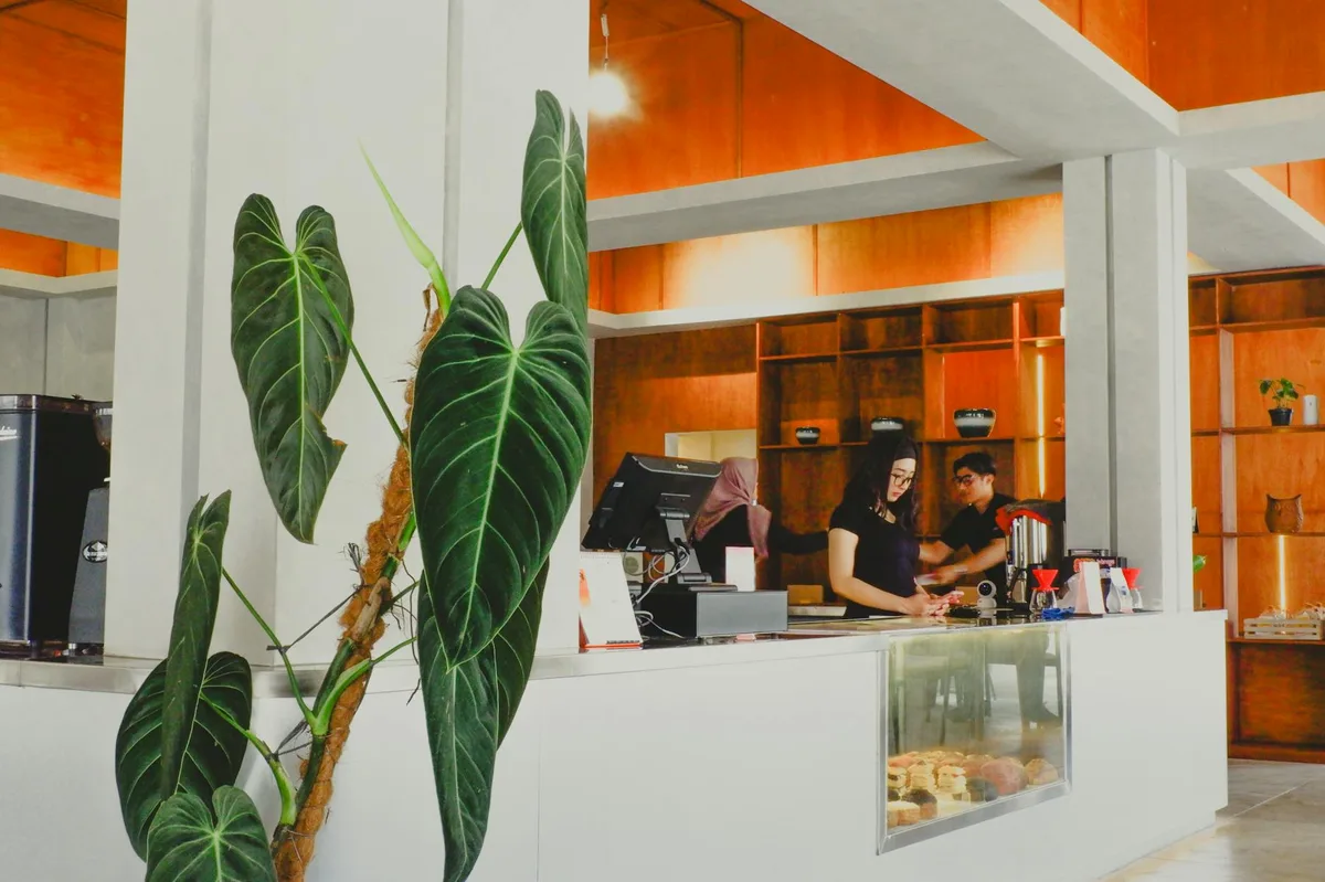 A stylish cafe interior in Indonesia featuring modern decor and lush greenery, creating a warm ambiance.