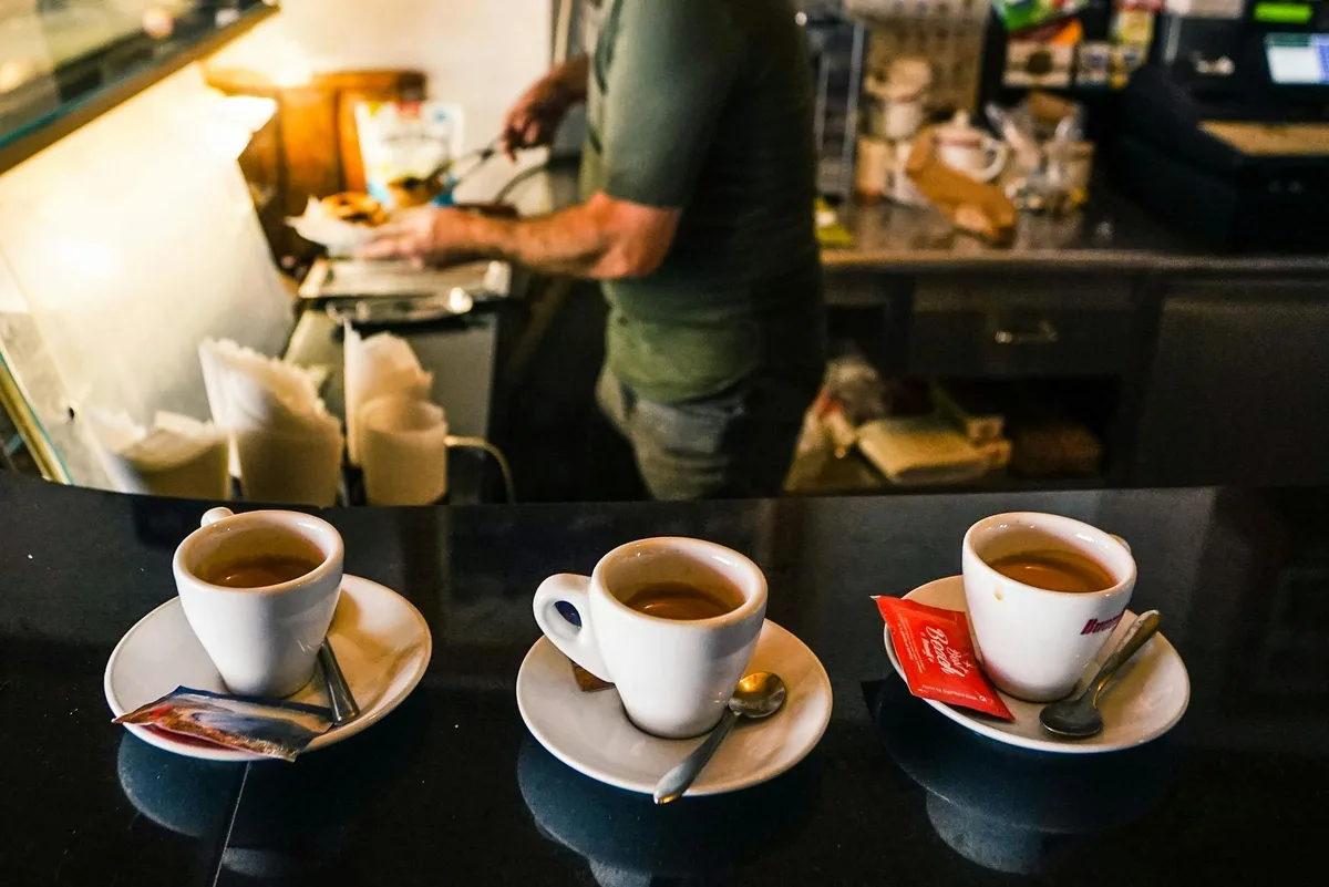 A barista in a café preparing espresso drinks on a countertop with three coffee cups in focus.