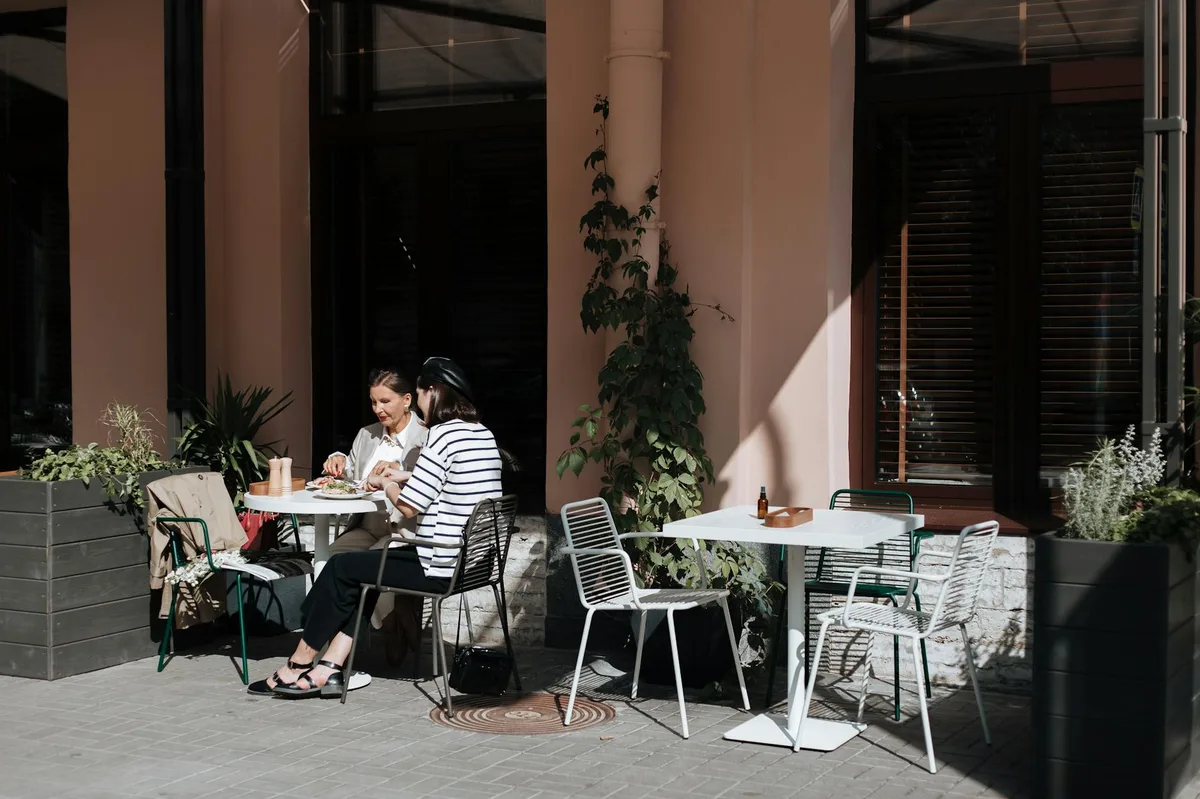 Two women enjoy an outdoor brunch at a charming cafe surrounded by plants.